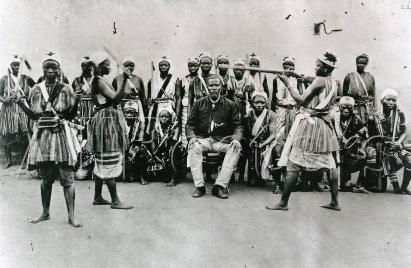 Historical picture of the Agodjie, circa 1890, author unknown. Several 
warrior women stand facing the camera, some sit down. The king sits in the center on his
throne